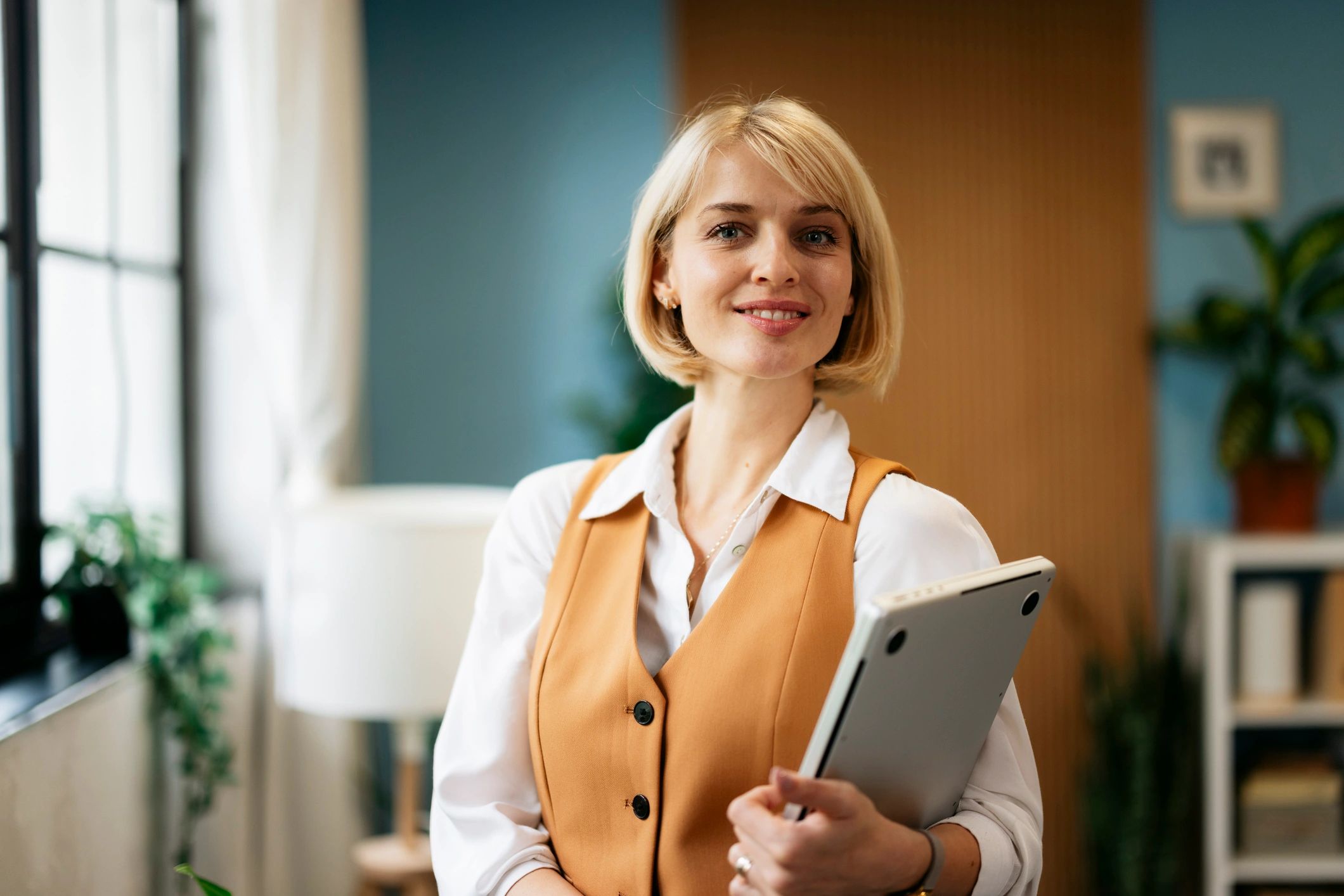 Confident young adult businesswoman holding laptop in office