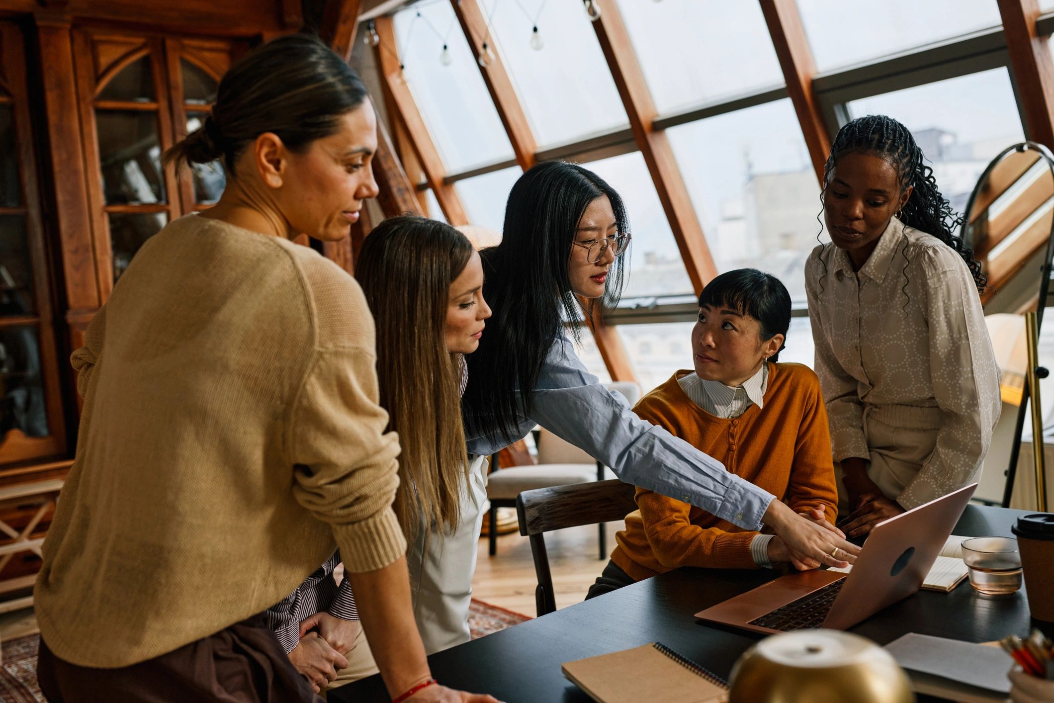 Multiracial women collaborating in a cozy office team meeting around a laptop